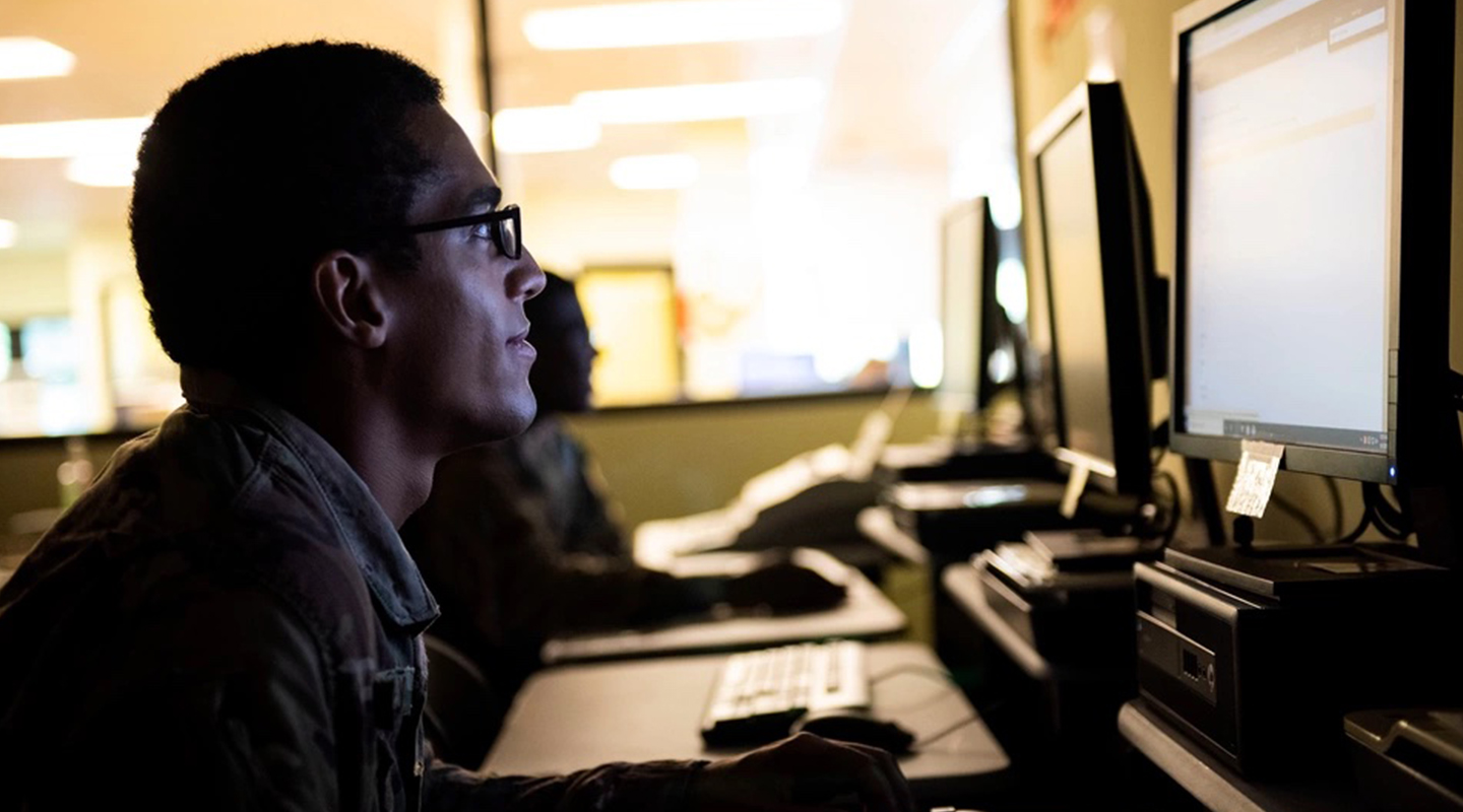 A Man Sitting At A Desk In Front Of A Computer