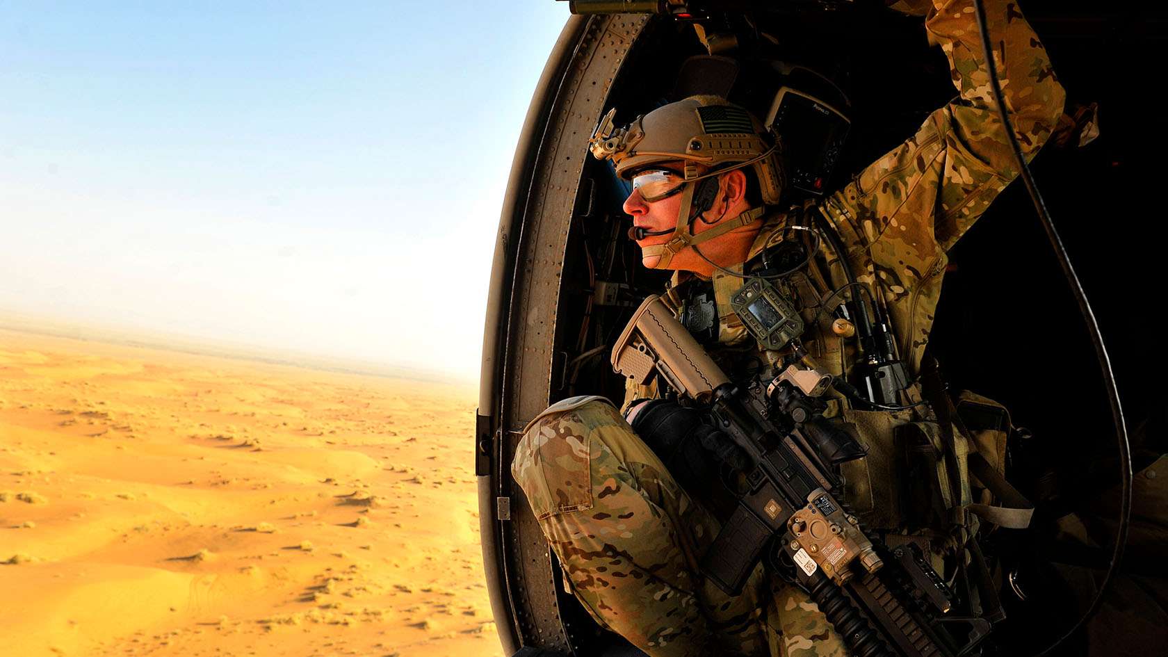 Combat Rescue Officer leaning outside a helicopter over the desert